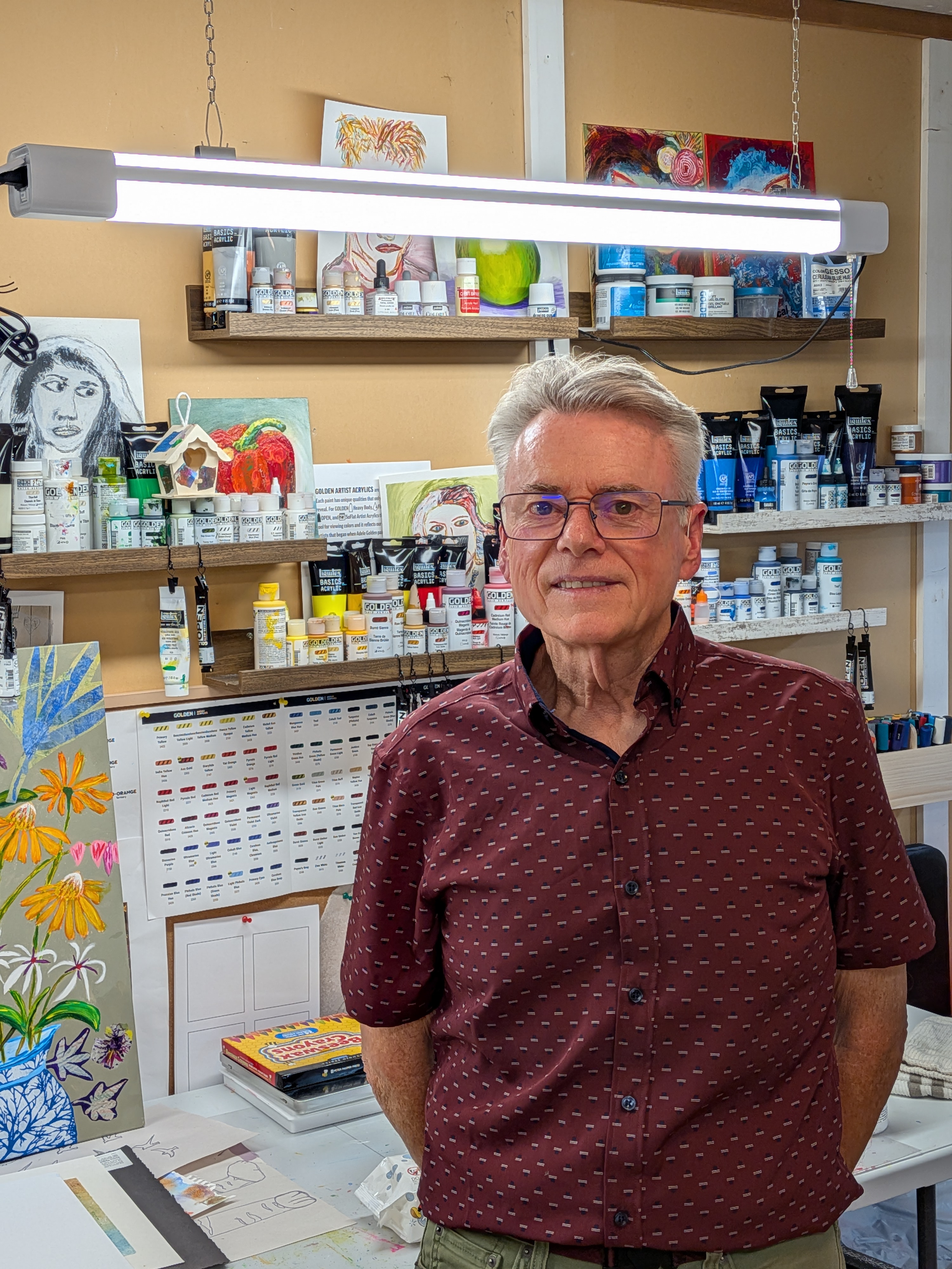 Portrait of Rick Rempel standing in his Saanich studio with a collage painting behind him
